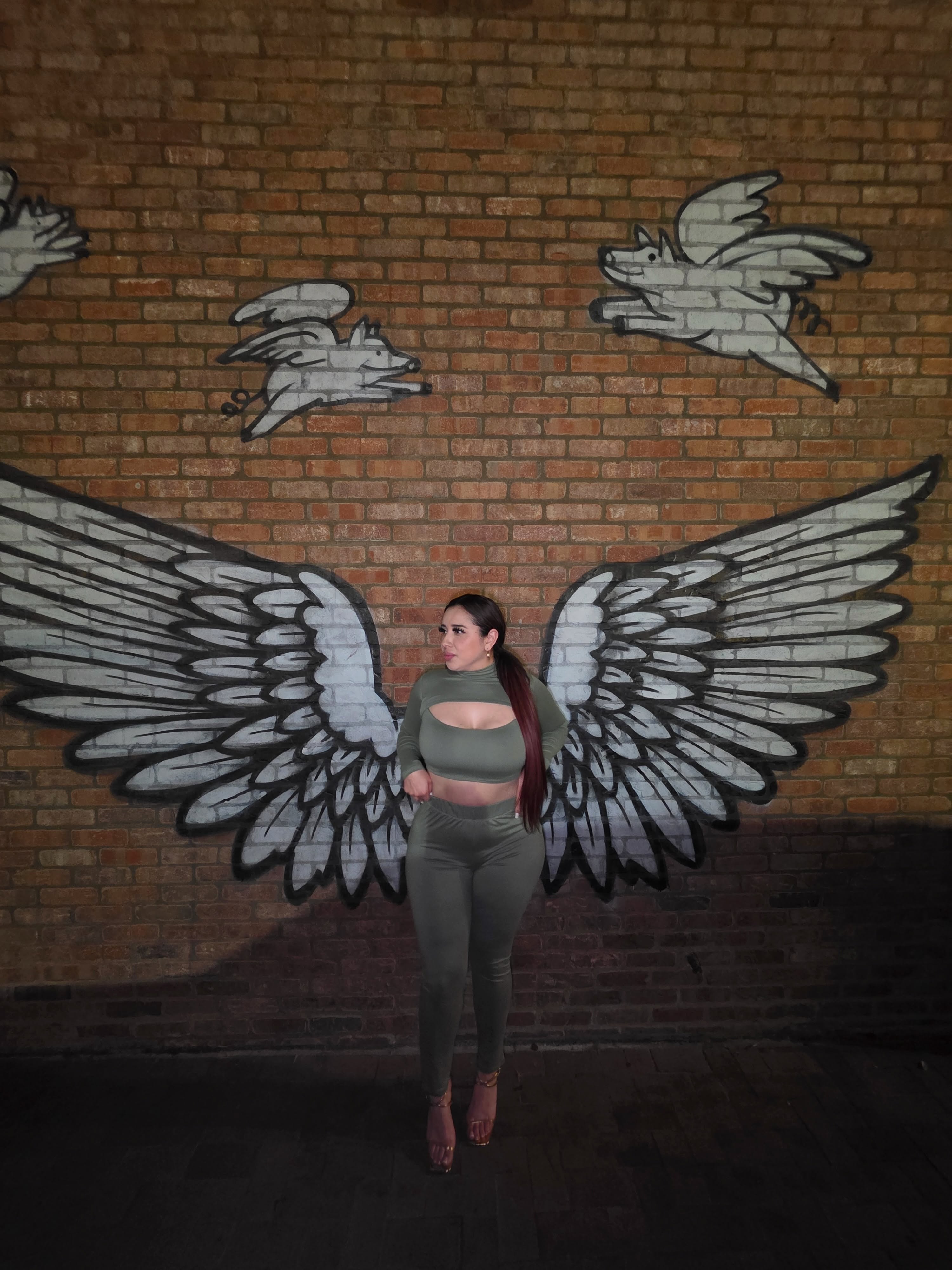 Wendy Estrada standing in front of a brick mural painted with large wings